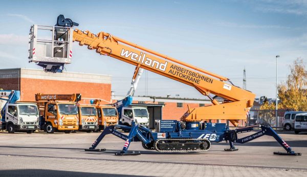 Kettenarbeitsbühne von Weiland mit ausfahrbarem Teleskoparm auf einem Industriegelände, ideal für präzise Höhenarbeiten.