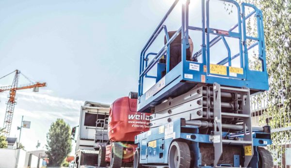 Weiland-Scherenarbeitsbühne und rote Gelenkteleskopbühne auf einem LKW beim Transport auf einer Baustelle.