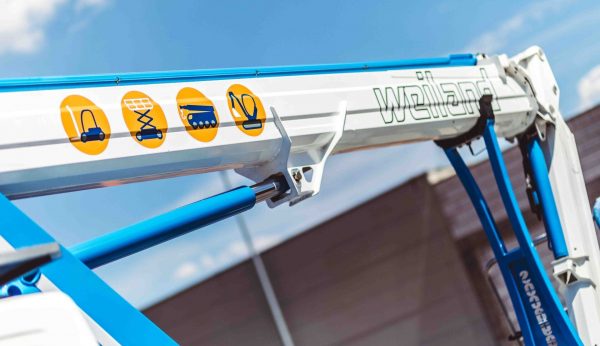 Detailaufnahme eines Weiland-Kranarms mit Piktogrammen für verschiedene Hebe- und Transportgeräte vor blauem Himmel.